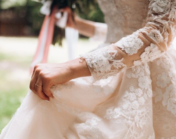 details-bridal-wedding-dress-hand-with-wedding-ring-outdoors-min